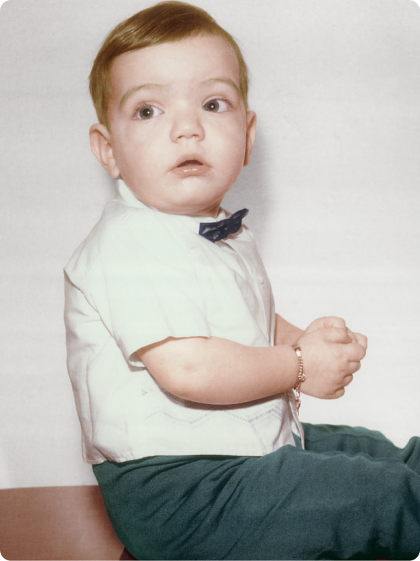Young child wearing a white shirt with rolled-up sleeves and green pants on a plain background